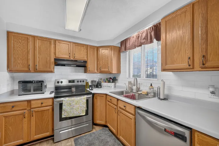 Galley kitchen featuring wood cabinetry, stainless steel appliances, a double basin sink, and white subway tile backsplash