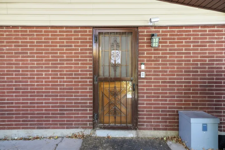 Red brick exterior with a security screen door, mounted outdoor light fixture, and exterior camera