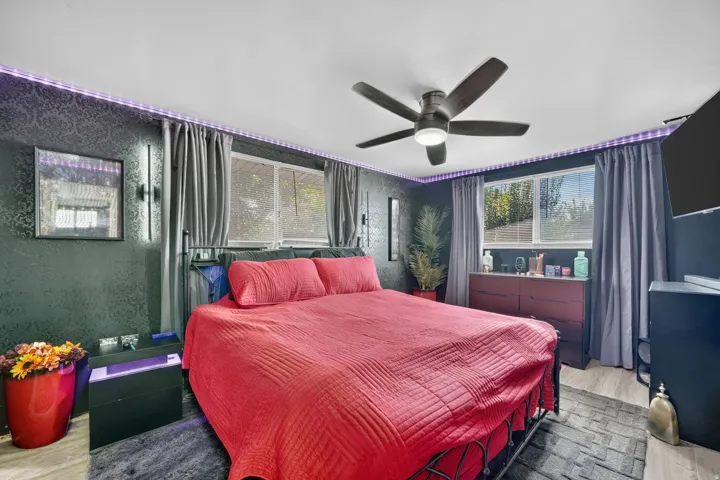 Wood-finish flooring, ceiling fan with integrated lighting, two windows with drapery, and accent lighting
