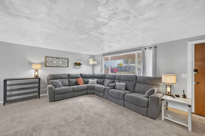 Light gray wall paint, textured ceiling, large window, and gray carpeting
