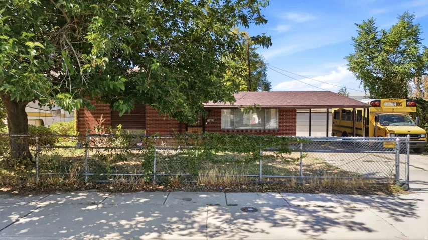 Red brick exterior with a brown shingle roof, chain-link fencing, and established trees