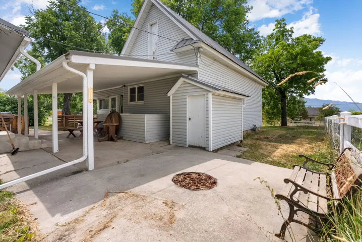 Carport structure with concrete pad, adjacent storage shed, and white siding