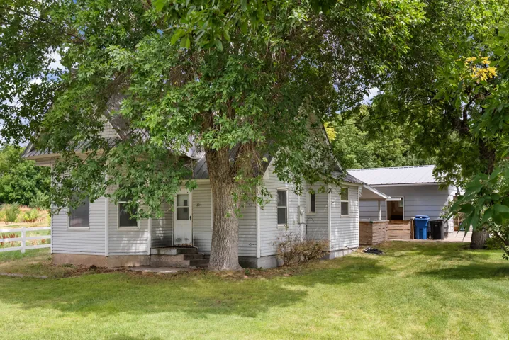 Lawn area with mature shade trees, white siding exterior, and a white fence