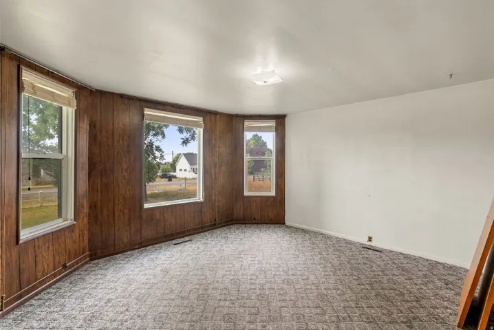 Wood-paneled accent wall with multiple windows, neutral wall paint, patterned carpet, and a flush-mount ceiling light