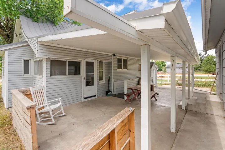 Covered concrete patio with siding exterior, multiple windows, and a built-in wood divider
