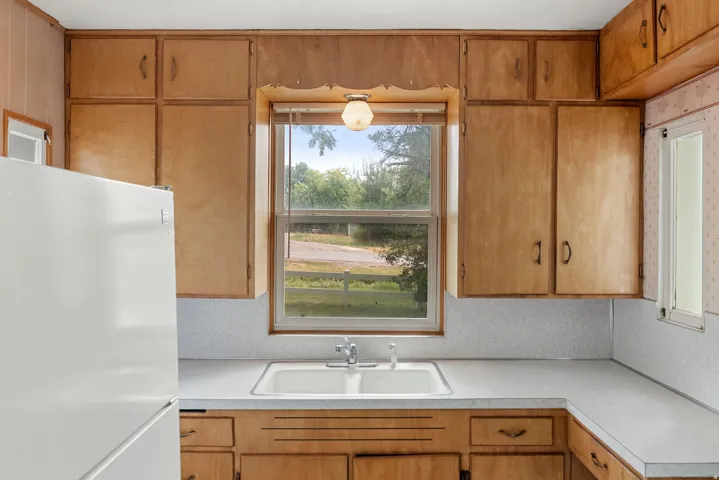 Wood-finish cabinetry providing ample storage, a window offering natural light, a dual basin sink, and a white countertop