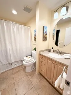 Ceramic tile flooring, built-in vanity with light wood finish cabinetry, composite countertop, and a circular wall-mounted mirror
