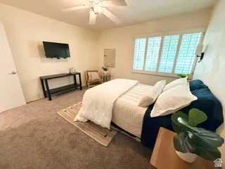 Neutral wall color, wall-mounted light fixture, ceiling fan, carpet flooring, and window with white plantation shutters