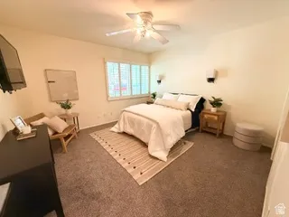 Carpeted room featuring a ceiling fan, wall-mounted lighting, and window with plantation shutters