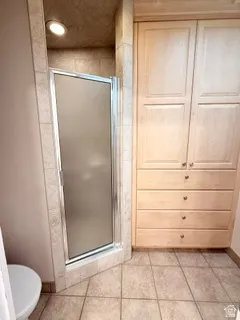 Tiled walk-in shower with a frosted glass door, recessed lighting, built-in cabinetry, and tile flooring