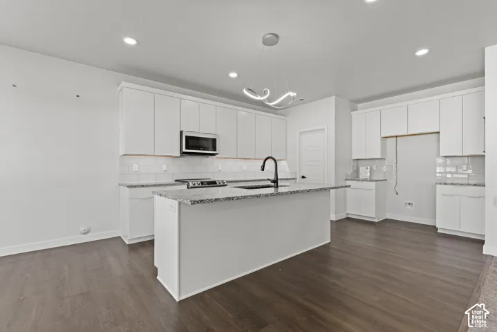 Kitchen featuring dark wood-finish flooring, white cabinetry, a large center island with a light-colored countertop, a stainless steel microwave, and a modern pendant light fixture