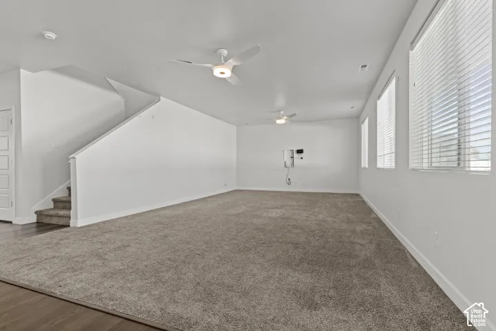 Expansive living space featuring plush carpeting, multiple windows with blinds, and two ceiling fans with integrated lighting