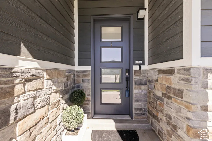 Contemporary entry door with square glass inserts and matte black hardware, framed by multi-tone stone veneer and horizontal siding