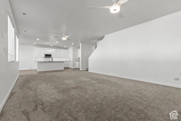 Open-concept living space with recessed lighting, ceiling fans, and a modern kitchen featuring white cabinetry, stainless steel appliances, and a central island