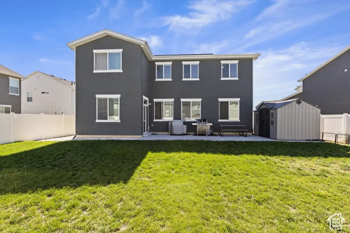 Rear exterior with dark stucco finish, white vinyl windows, a concrete patio, and a storage shed