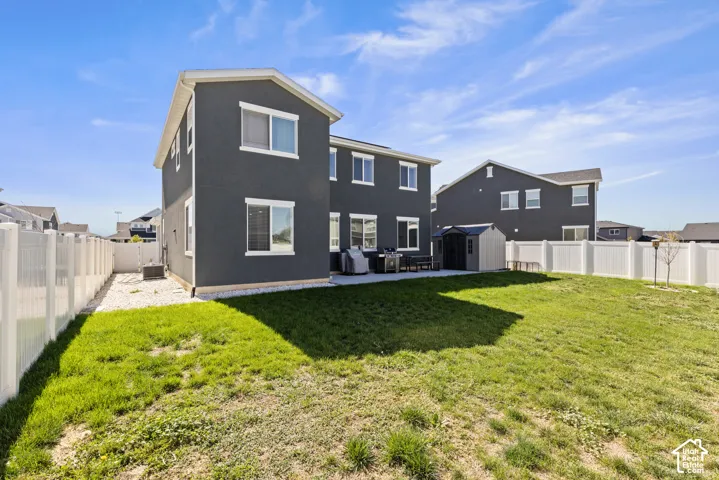 Expansive backyard featuring a manicured lawn, concrete patio, white vinyl fencing, and a storage shed