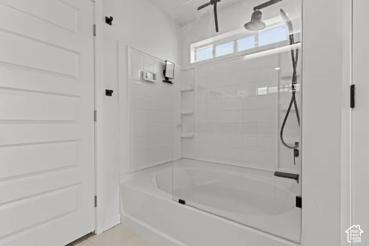 Bathtub with a glass shower enclosure, matte black shower fixtures, tiled surround, and transom window