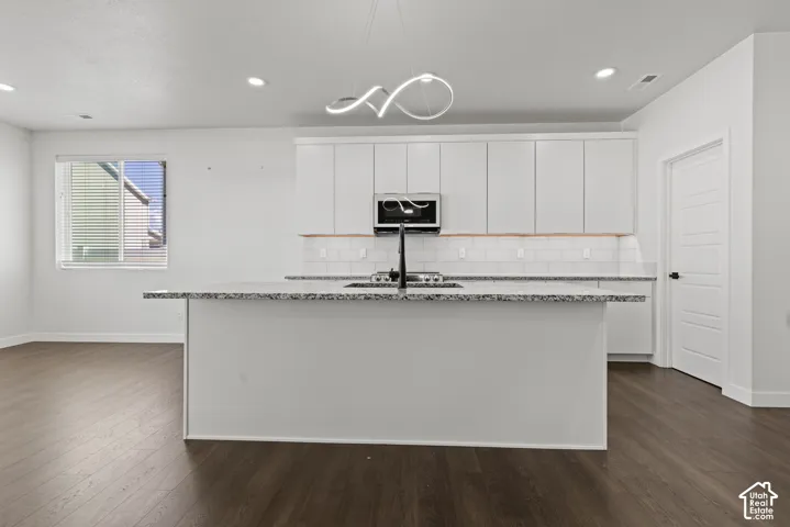 Modern kitchen featuring a large island with a patterned countertop, white subway tile backsplash, stainless steel microwave, and wood-finish flooring