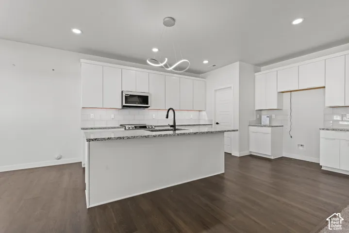 Spacious kitchen featuring an expansive center island, dark wood-finish flooring, white flat-panel cabinetry, stainless steel appliances, and a modern pendant light fixture