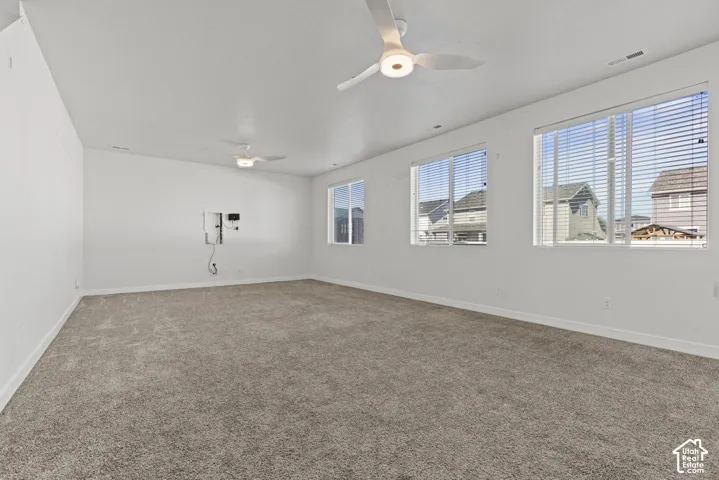 Expansive room featuring neutral-toned carpeting, multiple windows with blinds, and two ceiling fans