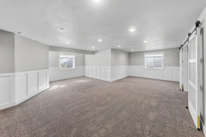 Spacious room with gray wall paint and white wainscoting, recessed lighting, and gray carpet flooring
