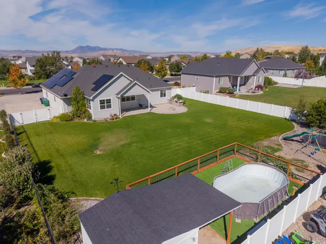 Expansive backyard with a manicured lawn, white privacy fencing, and a built-in fire pit