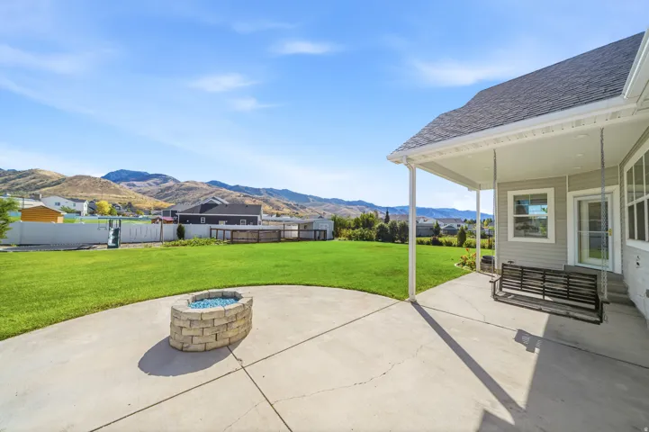 Expansive green lawn with a concrete patio featuring a built-in stone fire pit