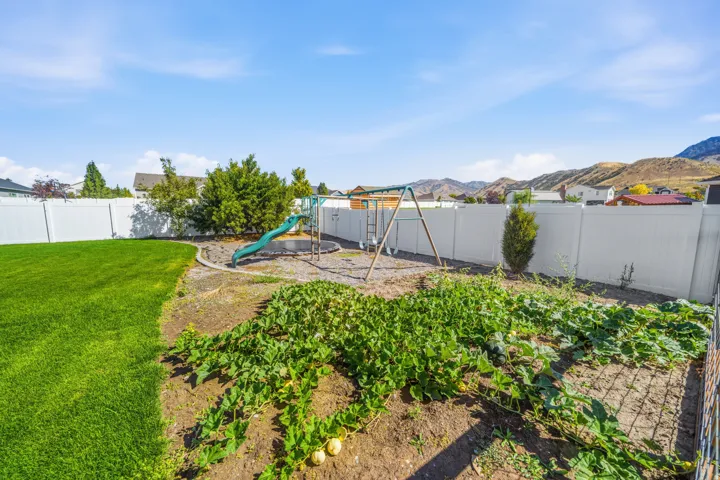 Expansive backyard with a manicured lawn, white privacy fencing, and a built-in garden area