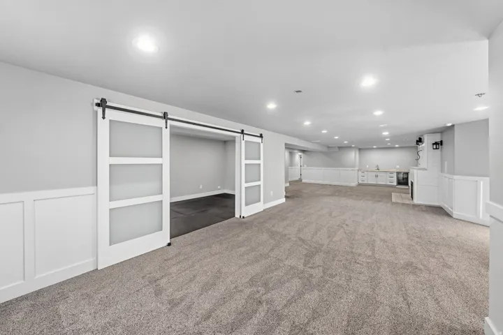 Spacious open-concept room featuring gray carpeting, recessed lighting, white wainscoting, and a built-in wet bar with cabinetry