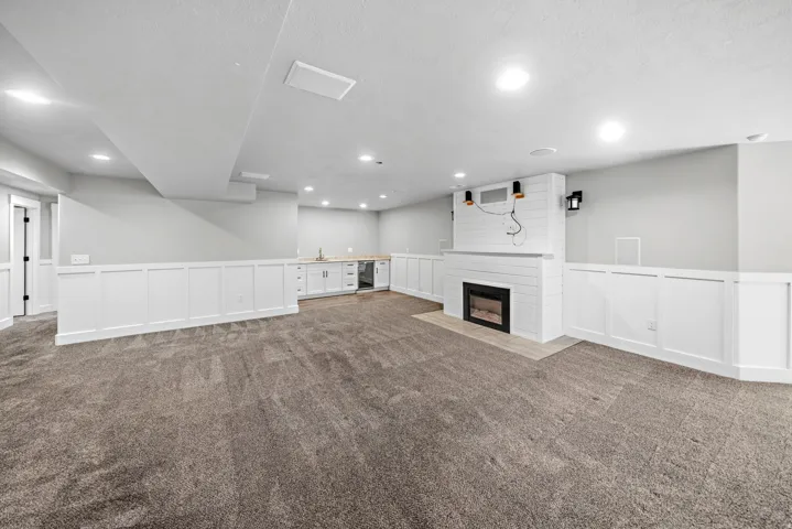Expansive living room featuring wainscoting, a fireplace with a shiplap surround, recessed lighting, and a built-in wet bar with a sink and cabinetry