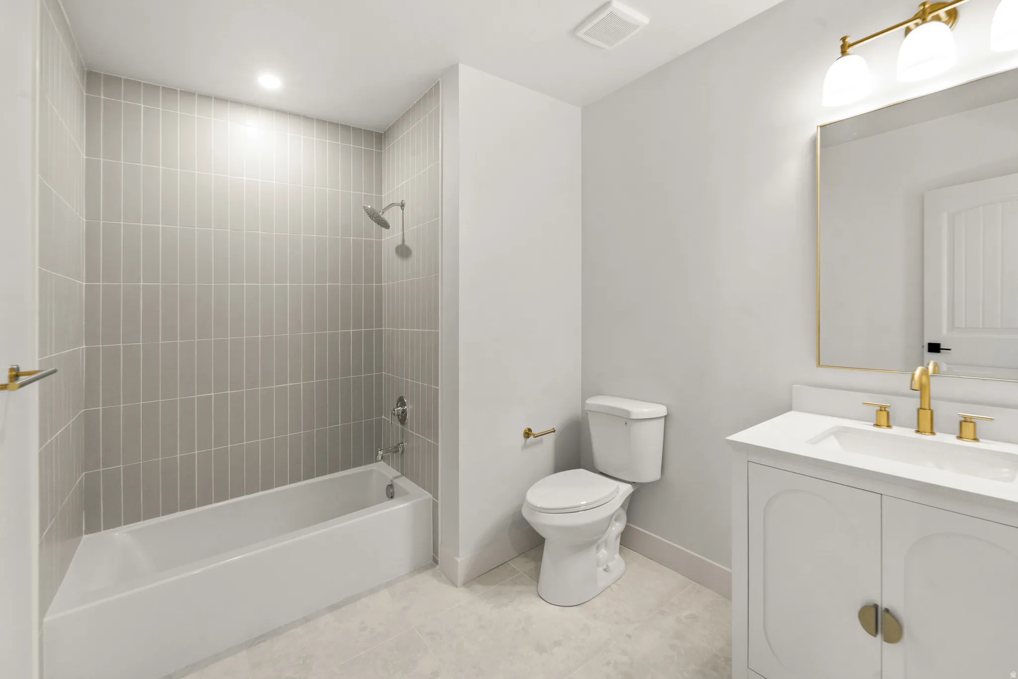 Bathroom featuring a white bathtub, gray vertical tile surround, white vanity with gold hardware, gold-framed mirror, and gold-finish faucet