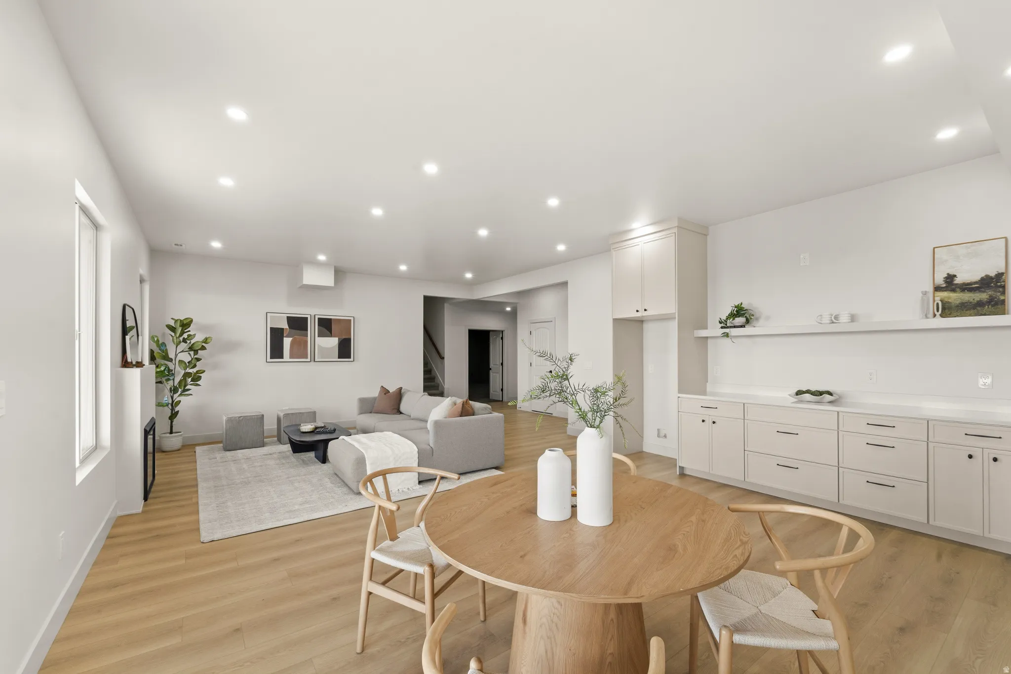 Open-concept living area featuring light wood-finish flooring, recessed lighting, white walls, and built-in cabinetry with shelving