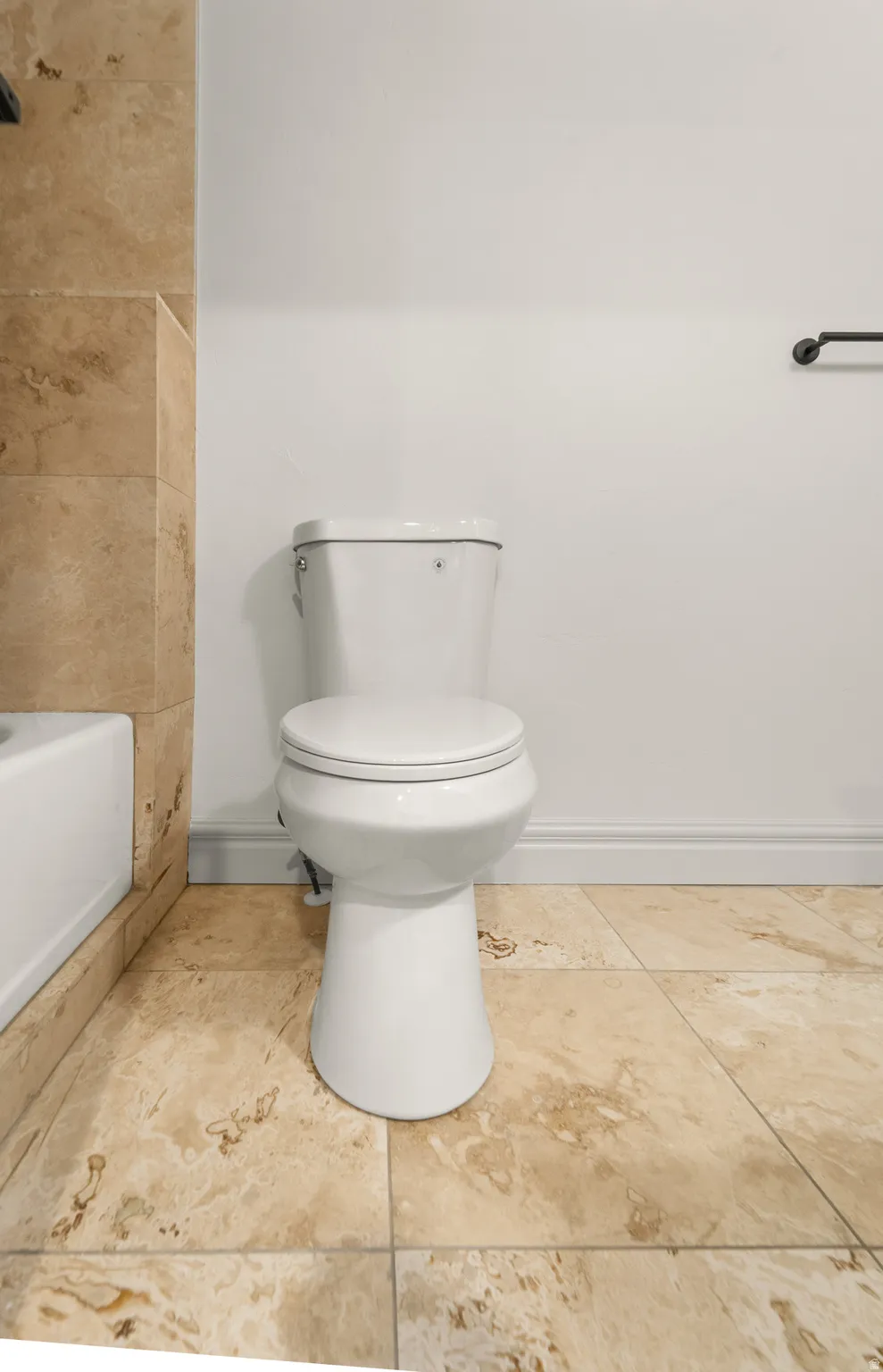 White toilet fixture with a two-piece design, complemented by large-format natural stone floor tiles