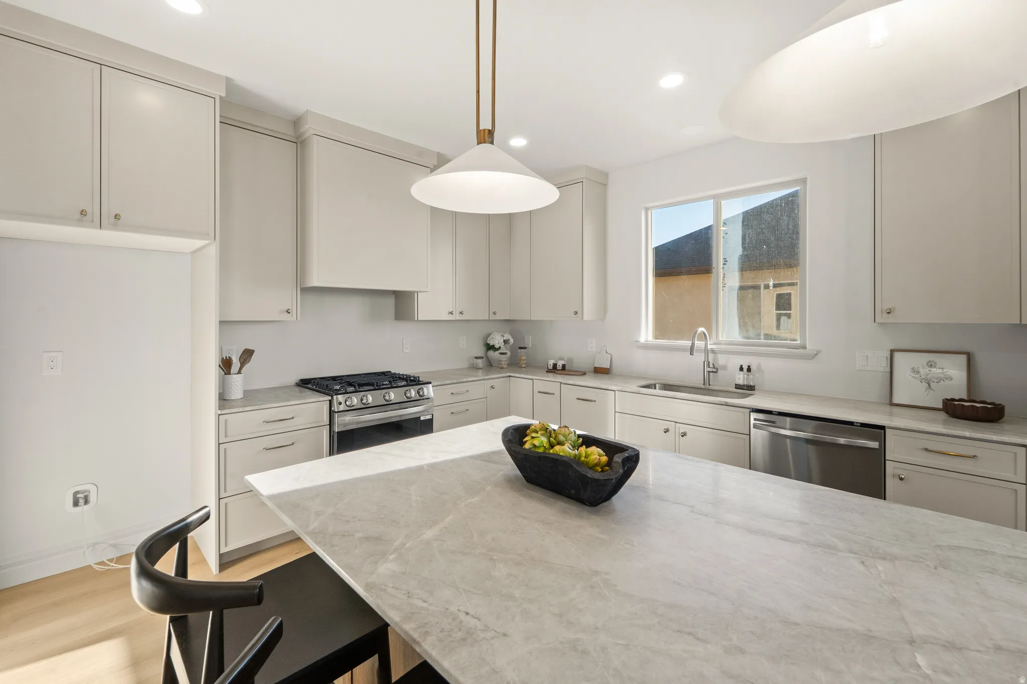 Kitchen featuring an expansive island with a light-toned countertop, light-toned cabinetry, stainless steel appliances, and wood-finish flooring