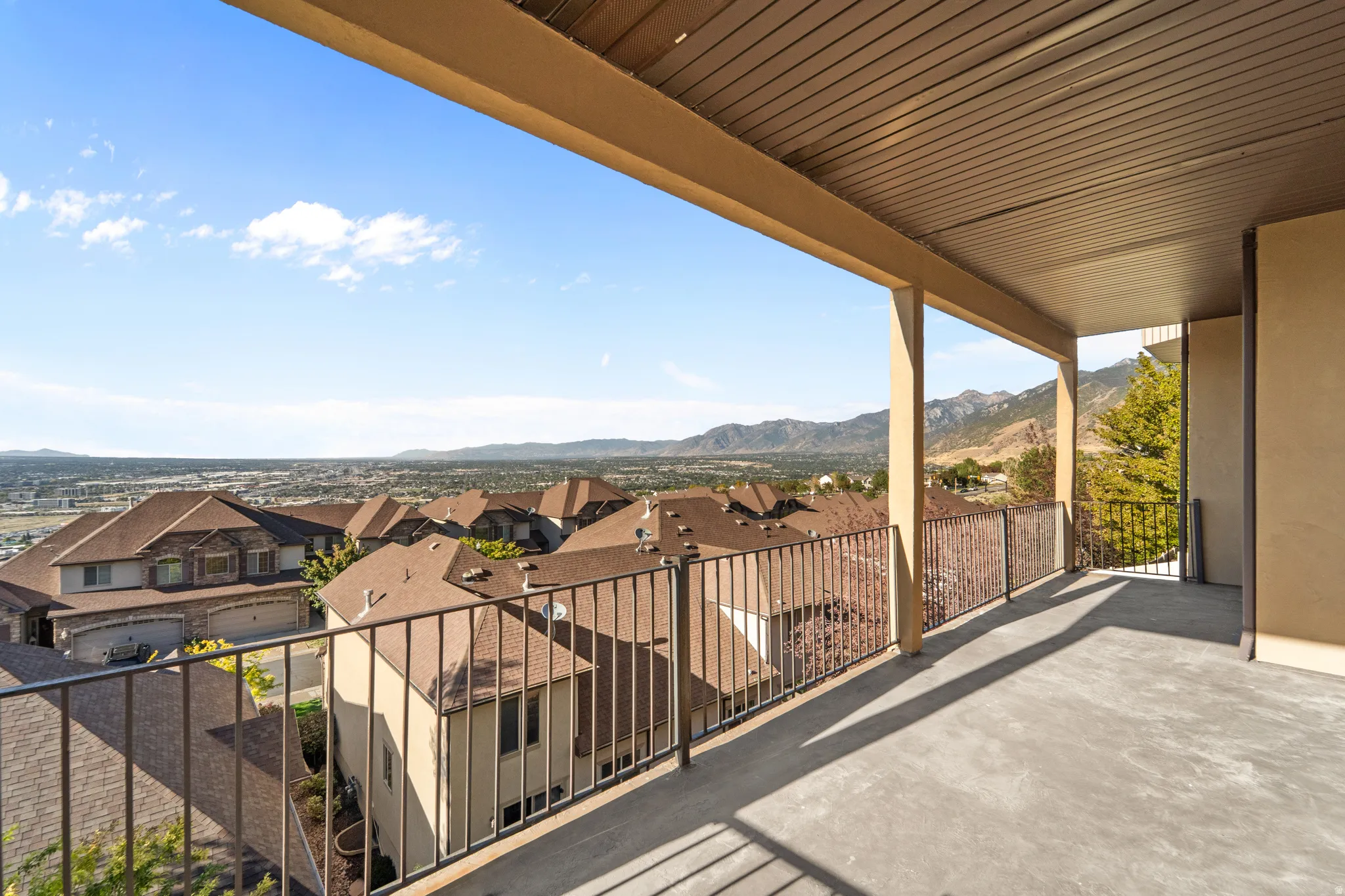 Expansive concrete balcony with metal railings and a slat-paneled ceiling, offering a mountain backdrop and cityscape scenery