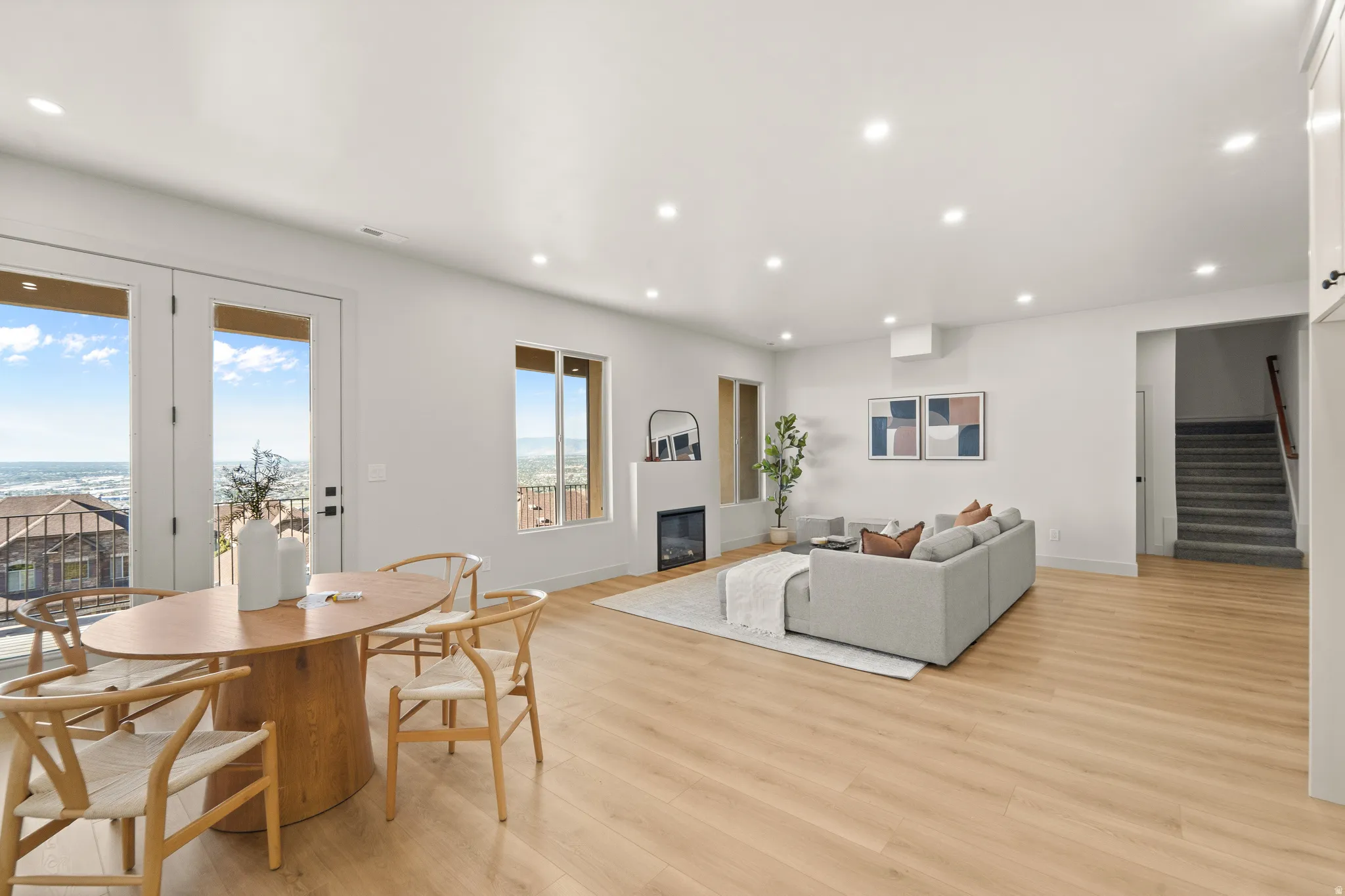 Open-concept living space with light wood-finish flooring, recessed lighting, and a modern fireplace