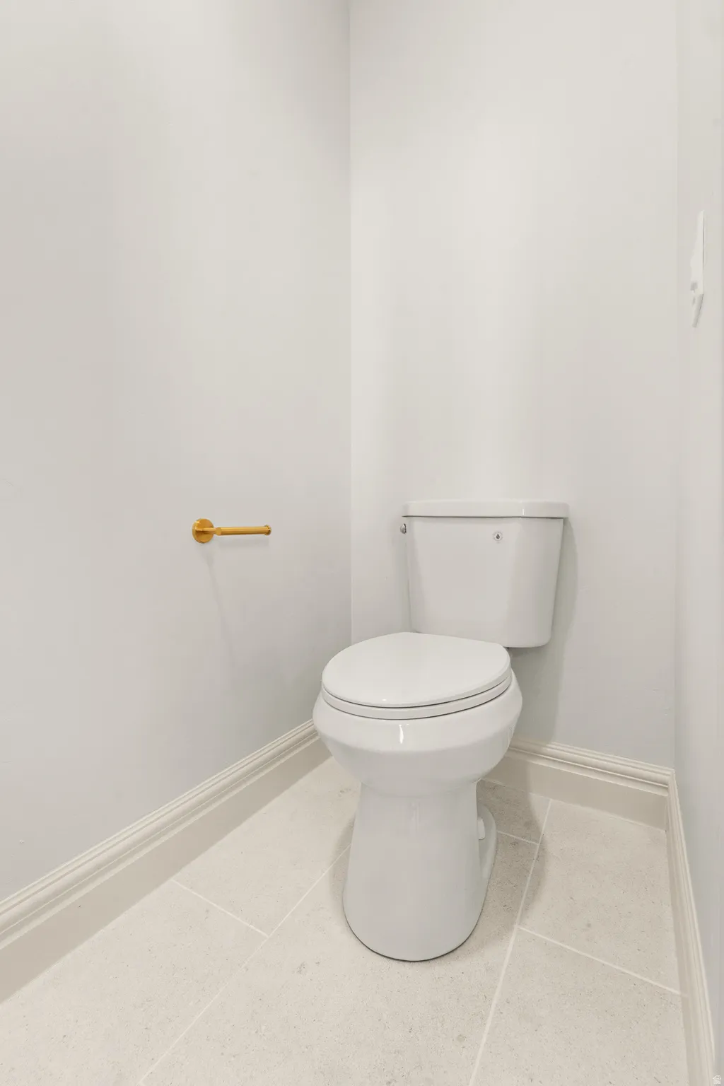 White toilet with a gold-finish toilet paper holder and light-toned tile flooring