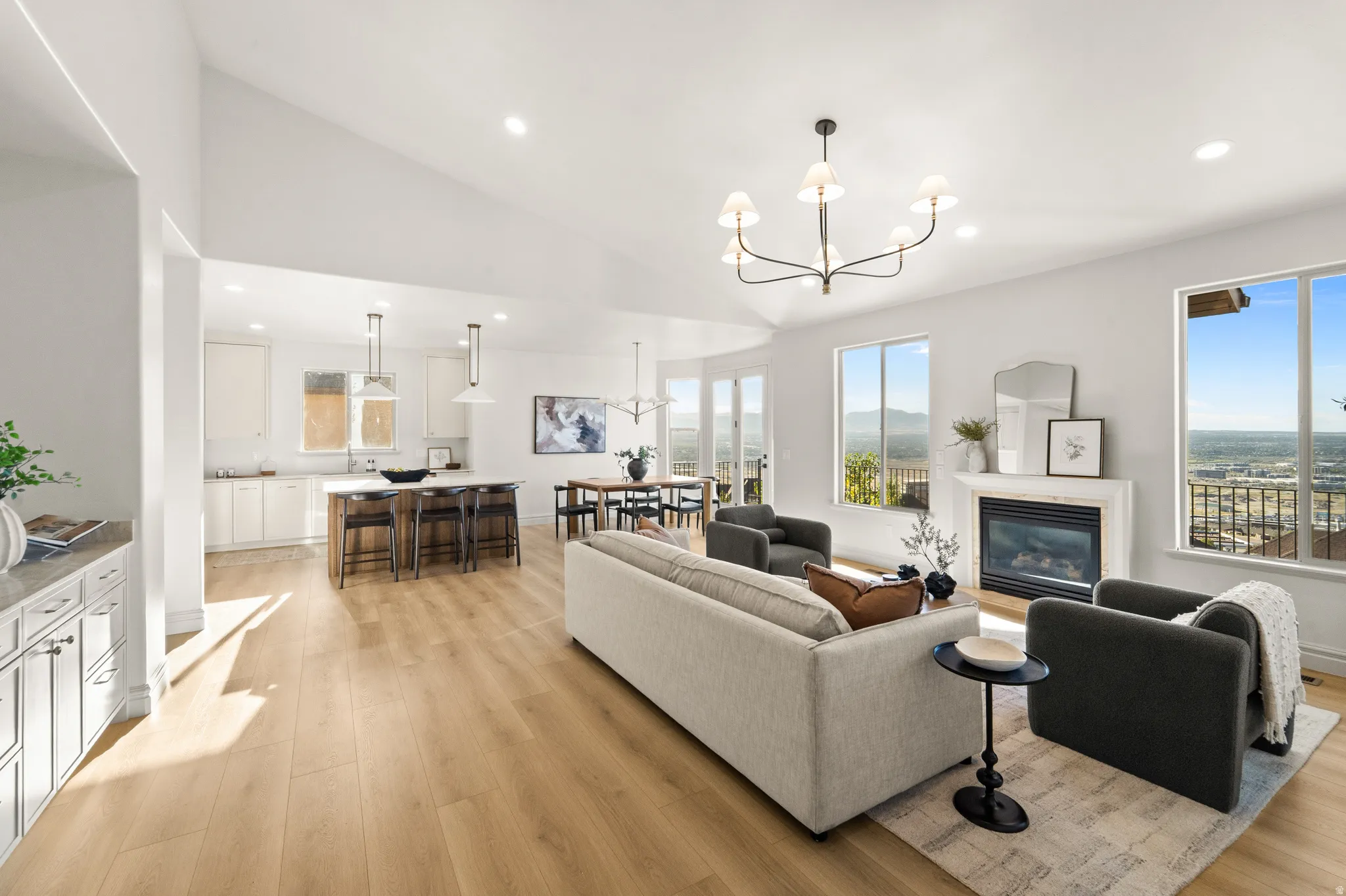 Vaulted ceiling with recessed lighting, light wood-finish flooring, built-in fireplace with white mantel, kitchen island with counter seating, and white cabinetry