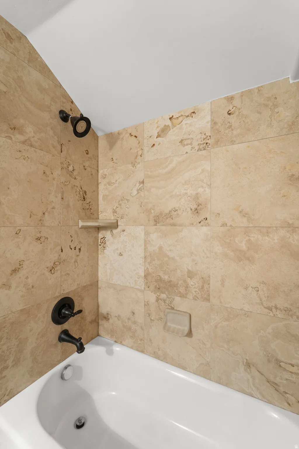 Alcove bathtub featuring a tile surround, built-in shelf, and dark-finish fixtures