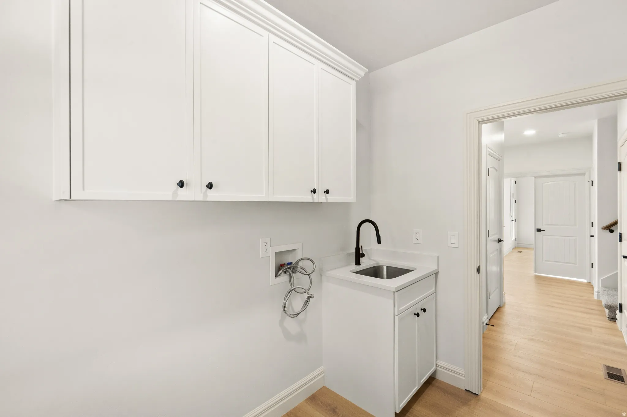 White shaker cabinetry with crown molding, a utility sink with a matte black faucet, and wood-finish flooring