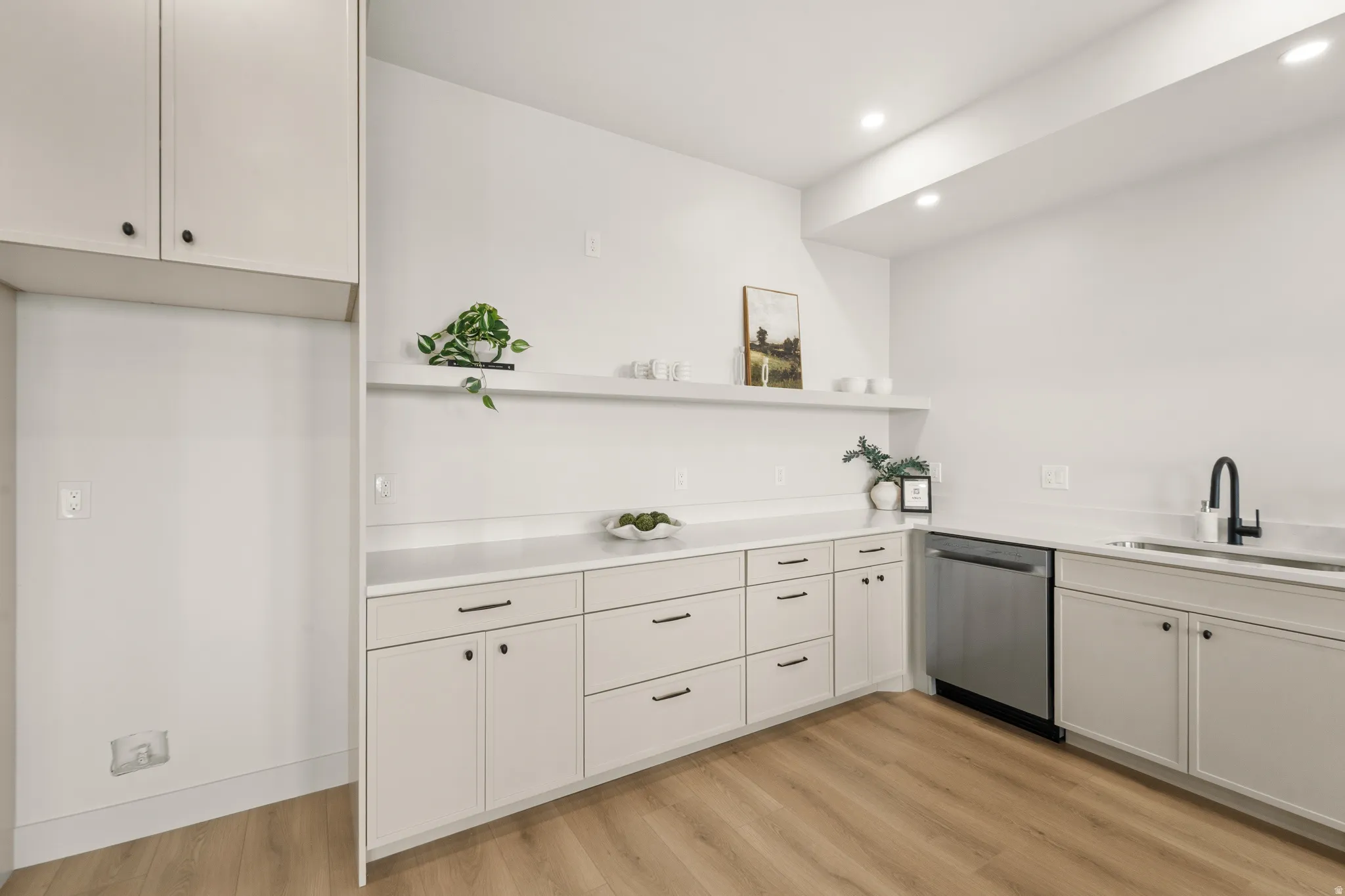 White cabinetry with black hardware, wood-finish flooring, recessed lighting, integrated stainless steel dishwasher, and a black gooseneck faucet