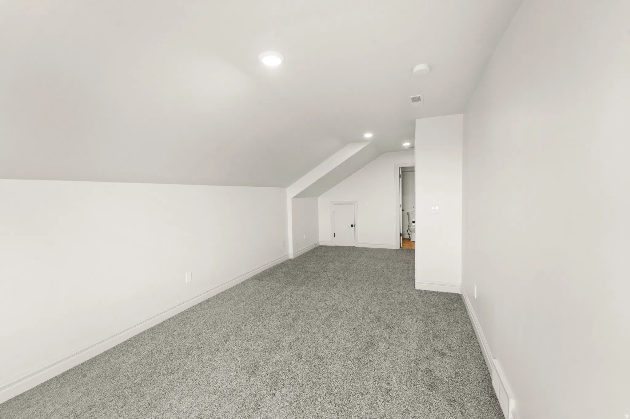 Sloped ceiling room featuring recessed lighting, a door with a black handle, and gray carpet flooring