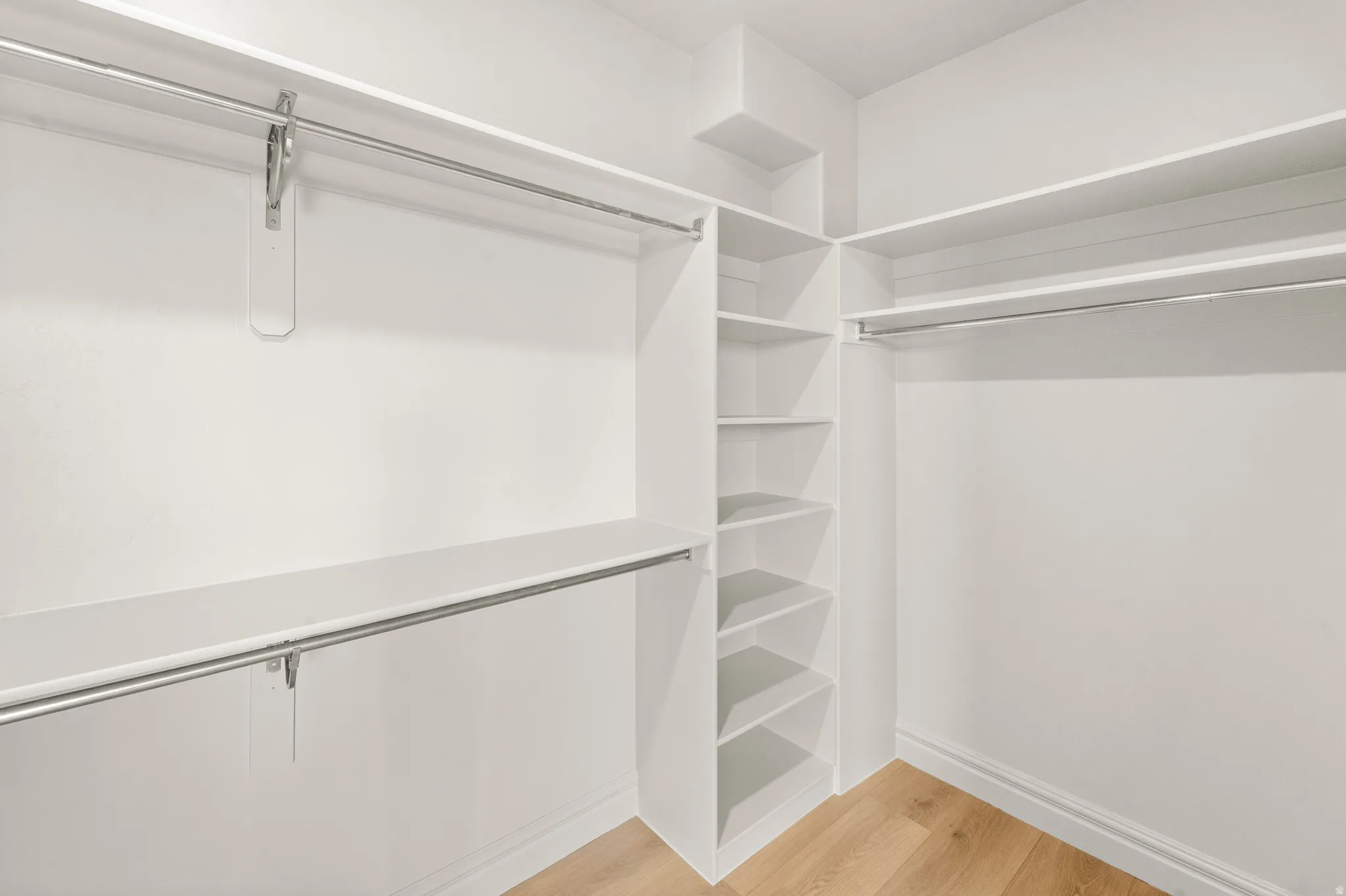 Custom closet system featuring multiple hanging rods, integrated shelving, and wood-finish flooring