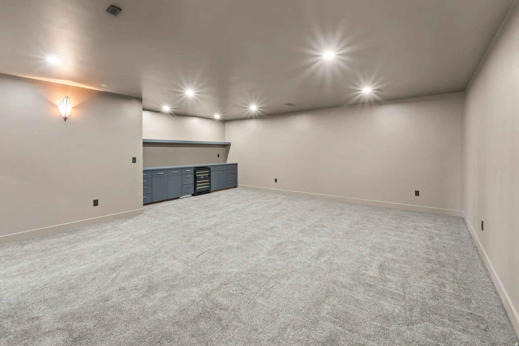 Expansive carpeted area featuring recessed lighting, built-in cabinetry, an integrated beverage cooler, and a wall sconce