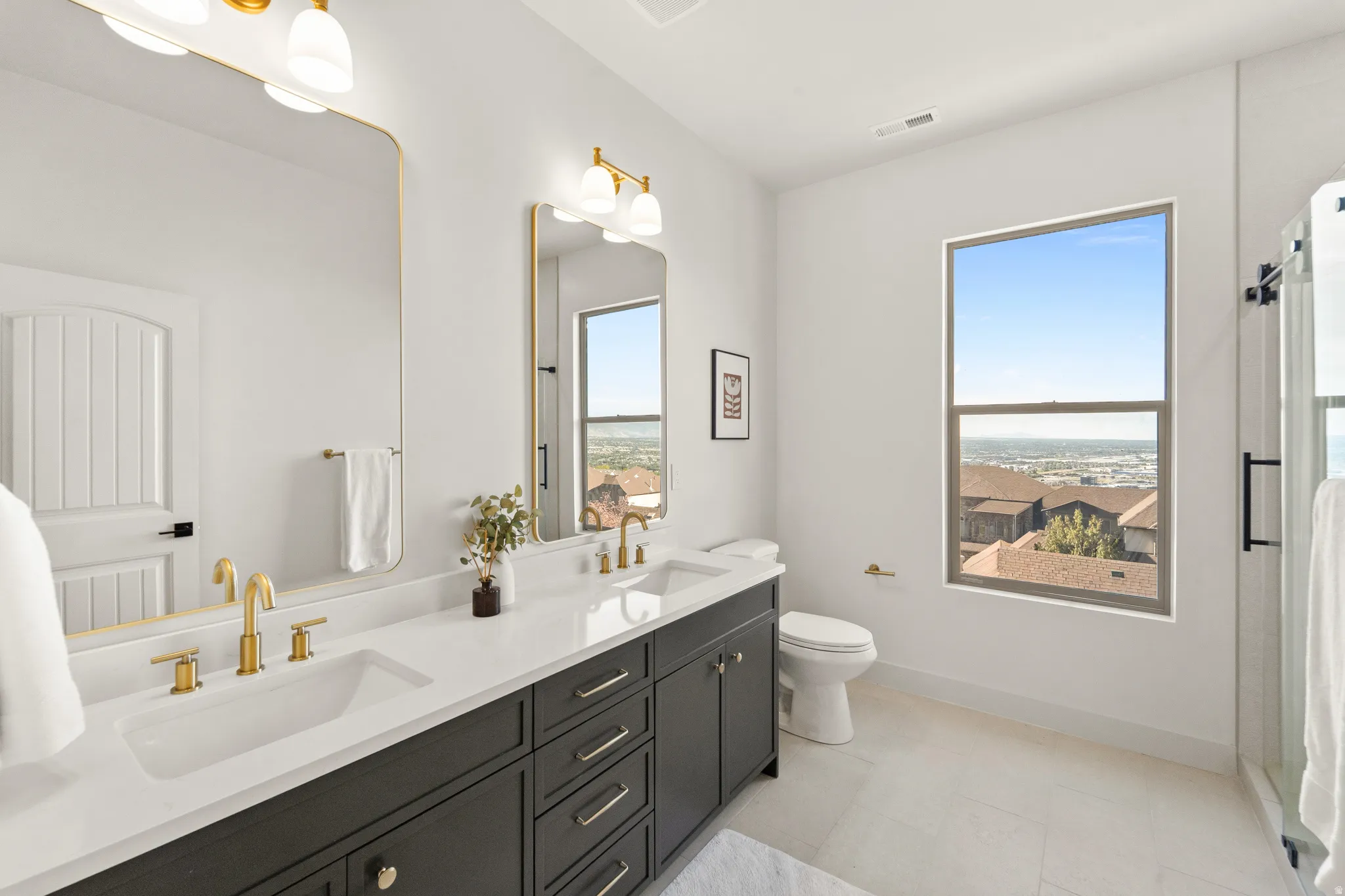 Dual vanity with gold-tone fixtures, white countertop, and dark cabinetry