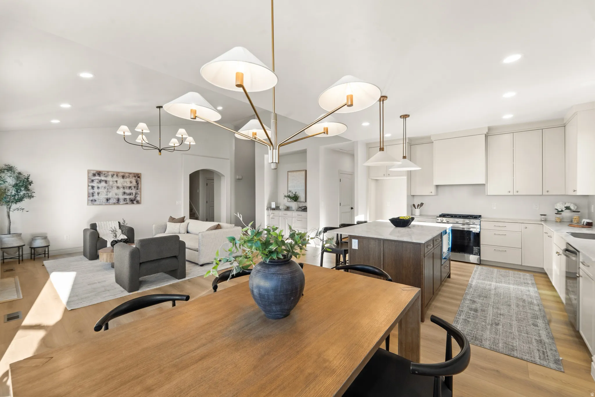 Spacious open-concept living area featuring a kitchen with a central island, stainless steel appliances, and shaker-style cabinetry, complemented by recessed lighting and a wood-finish flooring