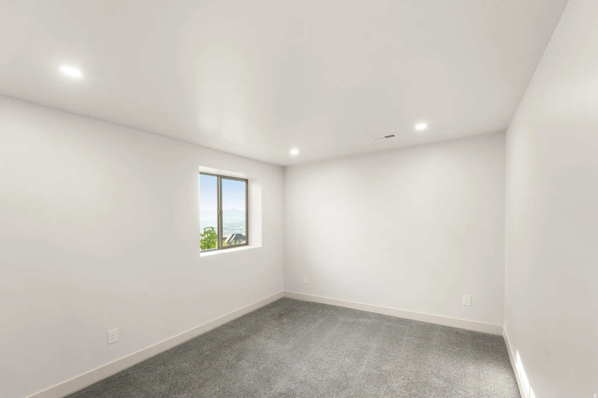 Recessed lighting illuminates this room, featuring light gray carpeting and white walls