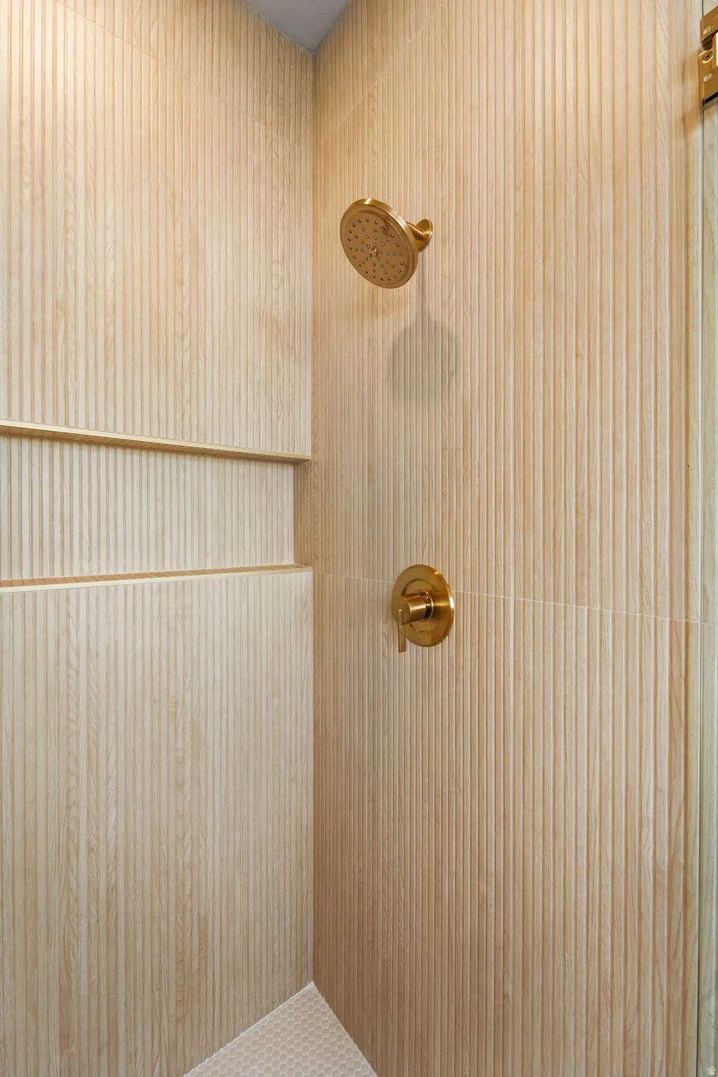 Shower with textured wall tiles, integrated niche, and brass fixtures