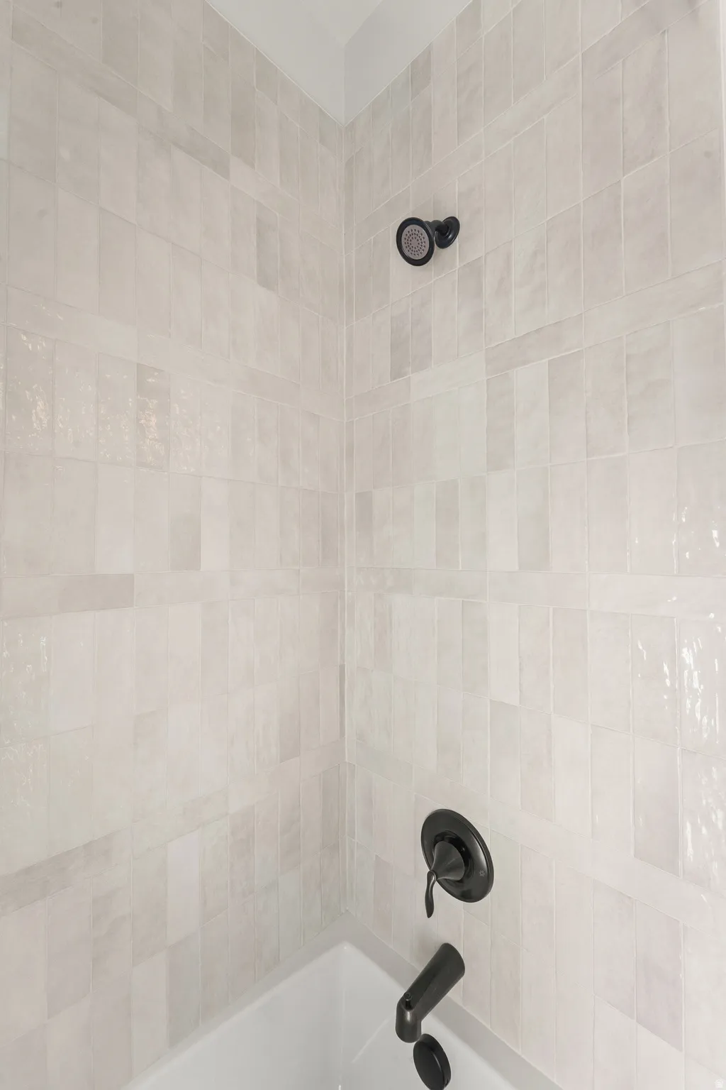 Bathtub shower combination with matte black fixtures and light-toned, rectangular wall tiles