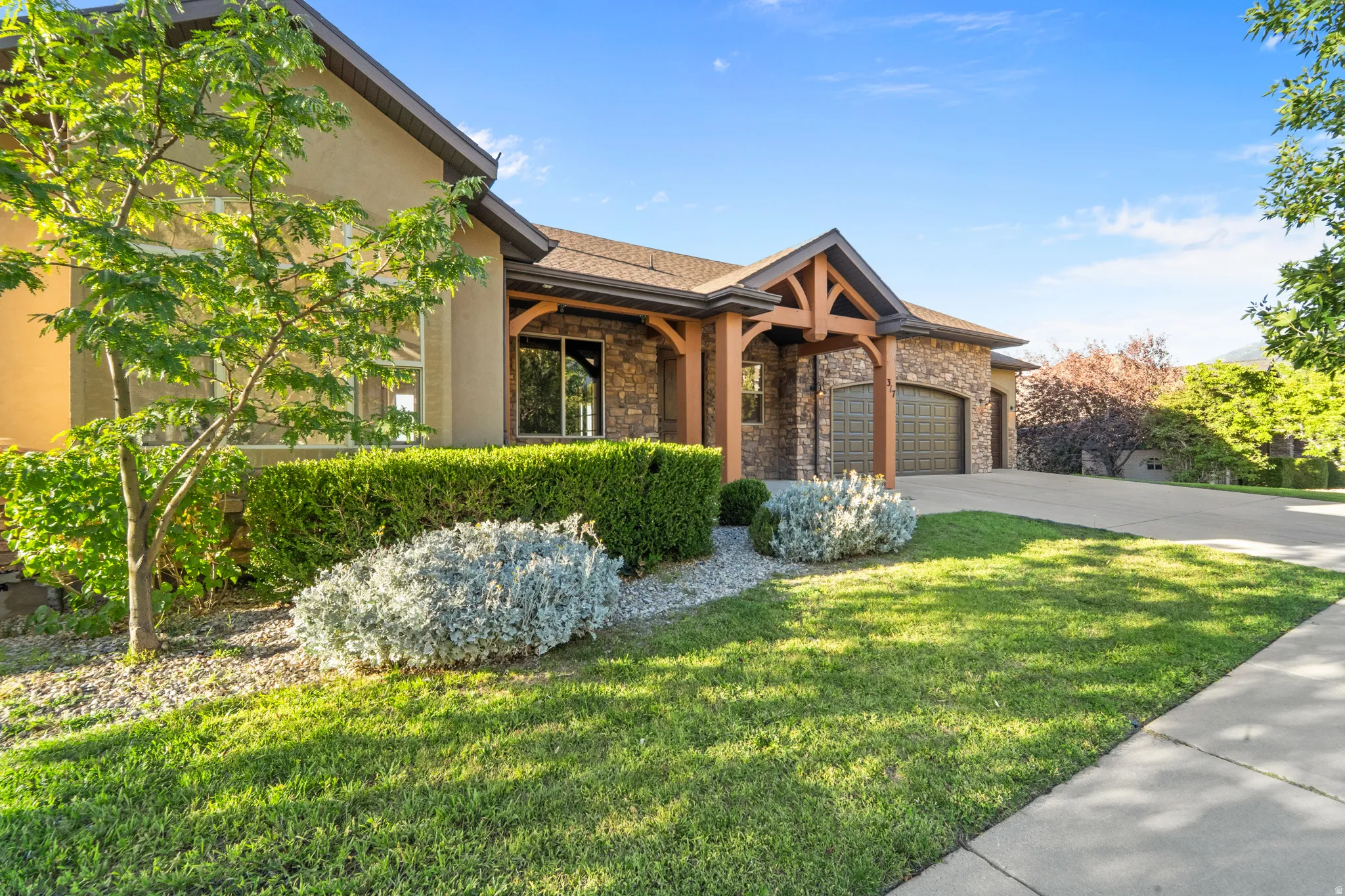 Stone and stucco exterior with exposed timber architectural accents, a paved driveway, and a two-car garage